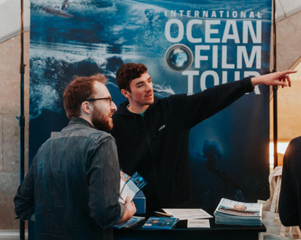 Stand van de International Ocean Film Tour met medewerkers die bezoekers informeren en brochures uitdelen.