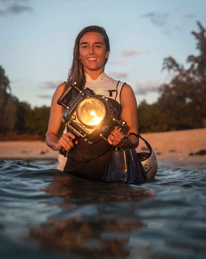 Surf photographer Christa Funk in the sunlight at the beach, holding her big underwater camera