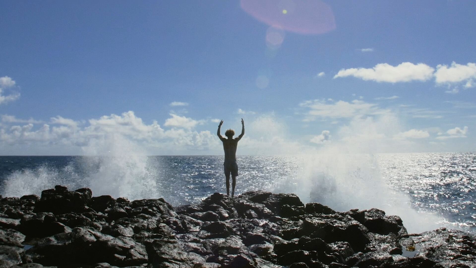 Man standing on a cliff, a wave lapping at the cliff